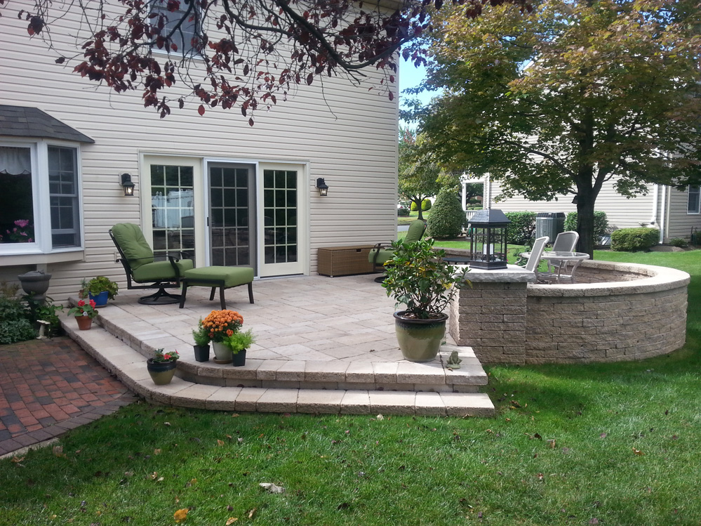 stone patio area of a home featuring a retaining wall, flowers & trees