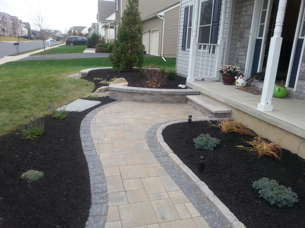 stone walkway leading to the front of a home with mulch next to it, tree planted